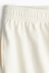 Pantalón deportivo de algodón color crudo, corte holgado, cintura elástica con cordón ajustable, bolsillos laterales y bajos sin rematar.