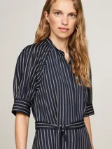 Vestido midi azul marino con rayas verticales blancas, corte amplio, mangas cortas raglán con puño, cuello mao, cierre de botones oculto, cinturón anudable y logo esmaltado de Tommy Hilfiger en el bajo.
