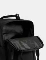 Mochila negra de tela deportiva con correas regulables, manijas superiores con broche, acceso con cierre superior y puller de cuerina, bolsillo frontal con cierre y puller de cuerina, y tag de goma.