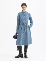 Tapado de cuero ovino color azul, con acabado símil denim. Tiene largo 7/8, cuello mao y cierre frontal con broches metálicos dorados y plateados. Incluye un lazo decorativo del mismo cuero en la cintura, mangas largas y vuelo hacia el ruedo. Cuenta con bolsillos ojal en los laterales.