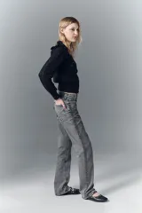 Jean tiro alto de denim negro rígido, lavado gris localizado con bigotes, pierna recta y apliques laterales de lentejuelas o tachas.