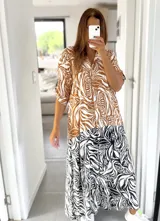 Vestido largo tipo camisero con estampado abstracto en tonos marrón, blanco y negro. Tiene cuello camisero, mangas 3/4 y cierre frontal con botones.