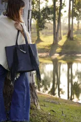 Bolso maxi negro de cuero con flecos y botón de guampa. Tiene bolsillo interior y cierre metálico.