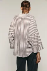 Camisa a rayas verticales color marrón y blanco, de corte holgado, con cuello solapa, cierre frontal con botones y mangas anchas por debajo del codo.
