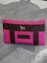 Sobre tipo cartuchera color borgoña, de lona con terminaciones en cuero marrón. Tiene cierre superior y aplique de cuero con el logo de la marca.