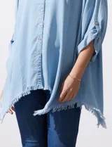 Camisa celeste de tencel, corte amplio, con cuello mao, escote en V y abotonadura frontal. Tiene bolsillos aplicados en el pecho, mangas 3/4 regulables con presilla y ruedo desflecado.