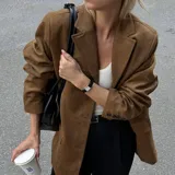 Blazer marrón de gamuza con cuello de solapa, cierre con botones y bolsillos frontales.
