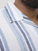 Camisa de manga corta a rayas verticales azules y blancas, con cuello resort y corte holgado.