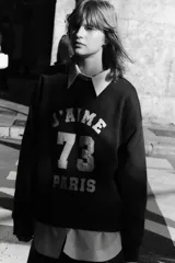 Buzo negro de corte oversized con interior cepillado suave, cuello redondo y mangas largas. Presenta un estampado frontal con el texto "J'AIME 73 PARIS" en color blanco.
