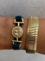 Pulsera con banda de terciopelo gris y apliques dorados con forma de moneda antigua.