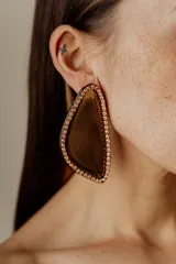 Aros colgantes con forma abstracta rellena de resina color marrón y bordes con strass color dorado.