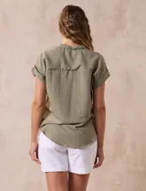 Camisa verde oliva de manga corta con cuello con solapa y abertura central con botones. Tiene un bolsillo aplicado en el pecho.