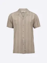 Camisa de manga corta color beige con rayas verticales en tonos marrón, negro y blanco. Tiene cuello tipo cubano y cierre con botones.