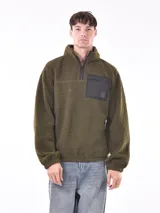 Buzo de polar verde oliva con cierre parcial y bolsillo de nylon negro en el pecho.