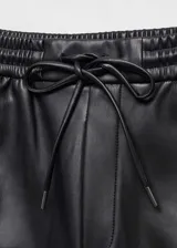 Pantalón negro de efecto piel, corte recto, tiro medio y cintura elástica con cordón ajustable.