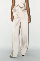 Pantalón de vestir color crema, de tela satinada, tiro alto y corte palazzo.