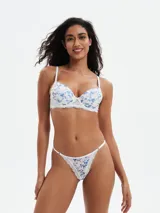 Tanga estampada con flores azules y celestes sobre fondo blanco, con detalles de encaje blanco.