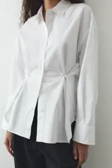 Camisa blanca de cuello solapa y manga larga. Detalle de pliegues con botones. Cierre frontal con botones.