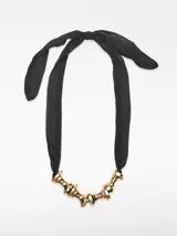 Collar con cinta de poliéster negra que se ata con un lazo y adorno central de piezas metálicas torneadas con acabado dorado.