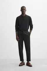 Pantalón negro de corte cropped, con cintura elástica ajustable con cordón, bolsillos laterales y traseros de vivo. El bajo tiene terminación con vuelta.