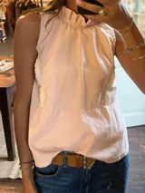 Camisa sin mangas color rosa pálido, con cuello alto fruncido y detalles de encaje color crema en los laterales. Corte holgado.