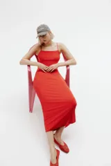 Vestido midi rojo de punto suave, corte entallado, con escote redondo profundo, espalda escotada y breteles spaghetti que se entrelazan en bucles y se atan en la espalda.