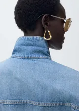 Chaqueta de jean celeste de corte oversize, con cuello camisero, cierre frontal con botones metálicos, dos bolsillos de parche con botón en el pecho y dos bolsillos laterales.