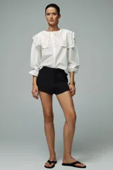 Camisa blanca de popelín de algodón con cuello redondo con tejido en superposición a tono y aplicación de bordados. Manga larga acabada en elástico y cierre frontal con botones ocultos por sopata.