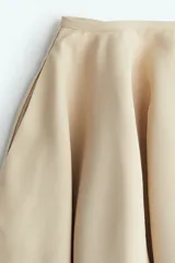Pollera mini circular color beige, con bolsillos laterales discretos y cierre oculto con corchete atrás.