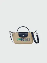 Bandolera Longchamp modelo Le Pliage Collection XS, color arena con detalles en azul marino. Presenta asa corta superior, correa larga ajustable y extraíble, cierre con solapa y botón a presión, y estampado frontal con logo y texto "Go The Extra Mile".