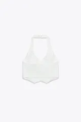 Chaleco blanco con cuello halter ajustable, escote pico, falsos bolsillos de vivo en delantero, detalle de costuras marcadas, forro interior a tono y cierre frontal con botones.