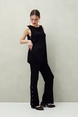 Pantalón negro de punto con calce relajado, caída fluida y botones dorados en los laterales.