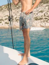 Short de baño azul con estampado de hojas en tonos verde y naranja. Cuenta con elástico en la cintura, cordón ajustable, tres bolsillos y mesh interior hipoalergénico.