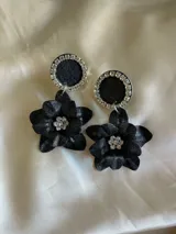Par de aros colgantes con base circular negra con borde de strass y dije de flor negra con centro de strass.