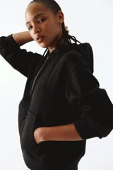 Campera con capucha negra en felpa con interior cepillado suave. Modelo con hombros caídos, capucha forrada en punto con cordón para ajustar, cierre y bolsillo canguro. Puños y bajo en punto elástico acanalado.