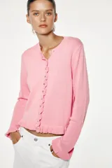 Chaqueta de punto rosa con cuello redondo y manga larga. Detalle de volantes en los bordes y cierre frontal con botones.