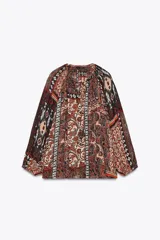 Blusa marrón con estampado de cachemir y detalles de hilo metalizado. Tiene cuello redondo con cordón ajustable y abalorios, escote en pico con nido de abeja, mangas largas con elástico en los puños y cierre frontal con botones forrados.