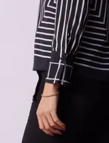 Blusa de gasa estampada a rayas verticales blancas y negras, marca Sioni. Tiene espalda con abertura y botón, y mangas largas con puño y botón.