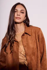 Camisa color marrón de gamuza sintética, con cuello clásico, cierre frontal con botones y mangas largas con puños abotonados.
