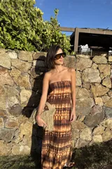 Vestido strapless largo con estampado batik en tonos marrones y beige, entallado al cuerpo y con espalda baja descubierta.