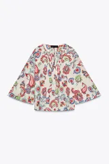 Camisa de algodón color crudo con estampado de cachemir en tonos rojo, azul y verde. Tiene cuello redondo, escote en pico, manga tres cuartos acampanada y bajo asimétrico redondeado.