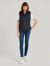 Chaleco acolchado azul marino con capucha ajustable con cordones y cierre de cremallera frontal. Bolsillos laterales con cremallera y logo de Tommy Hilfiger bordado en el pecho. Detalles distintivos de Tommy Hilfiger en el ruedo.