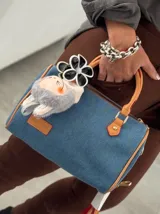 Cartera tipo bowling de jeans azul con detalles en cuero sintético color camel. Incluye llavero de peluche y dije de flor.