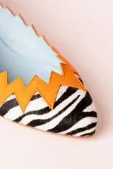 Bailarinas con estampado animal print de cebra, puntera fina y detalle de ante naranja en zigzag en el borde superior. Interior celeste y suela de cuero.