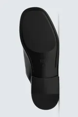 Zueco negro de cuero con punta redondeada y suela plana.