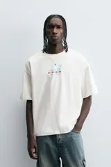 Camiseta color crudo de corte relajado, cuello redondo y manga corta. Estampado frontal con texto "Flies to Los Angeles CA" y diseño de bandera a cuadros.