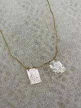 Collar dorado con cadena fina y dos dijes rectangulares de nácar con grabados religiosos.
