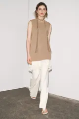 Vestido color beige, de corte recto, con cuello redondo y sin mangas. Presenta un tejido de punto en la parte superior y un volante de encaje blanco en el ruedo.