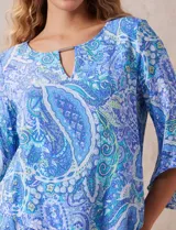Blusa de gasa estampada con motivos paisley en tonos azules, marca Ruby Rd. Tiene cuello redondo con escote en V y aplique metálico. Presenta una sobre capa delantera y terminación asimétrica. Las mangas son 3/4 y amplias.