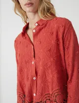 Camisa de algodón color naranja, con bordado suizo y encaje calado. Tiene cuello con solapa, botones frontales, mangas largas con terminación de encaje y ruedo asimétrico con galón de encaje.